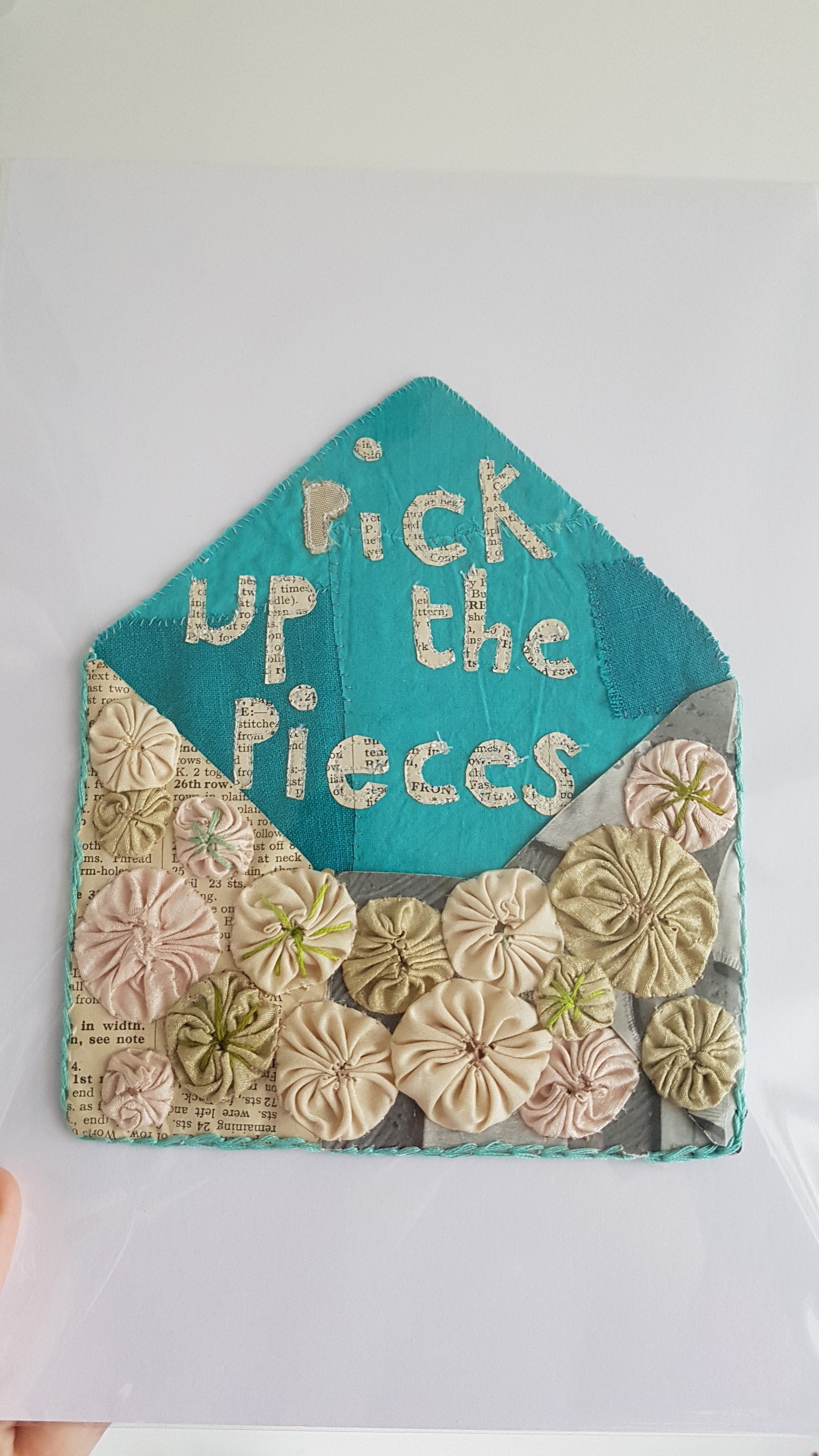 Textile art evelope with Pick up the Pieces witteh in paper applique. Embellished with silk suffolk puffs otherwise known as yoyos.