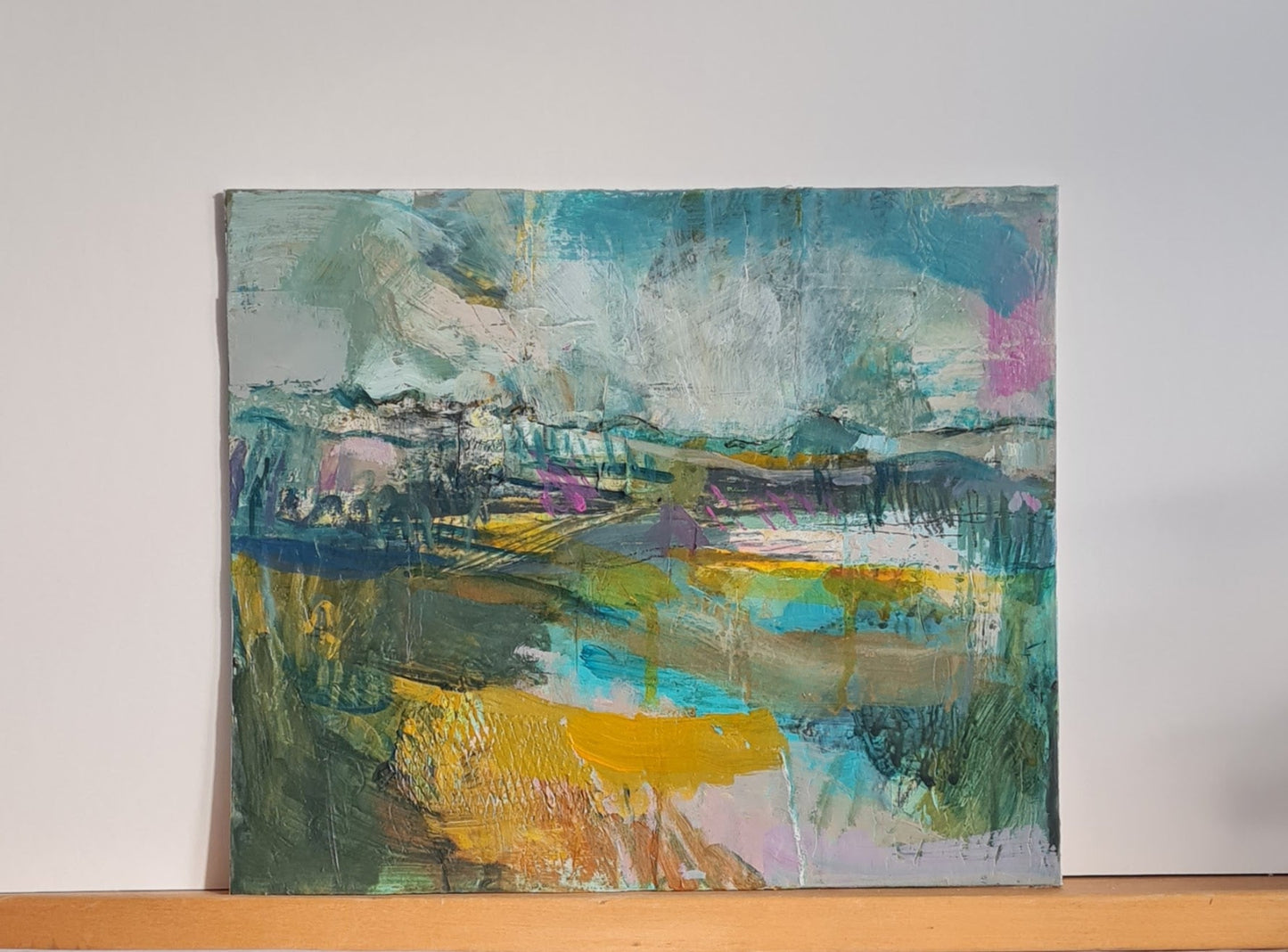 Abstract painting on a white wall with a wooden shelf below