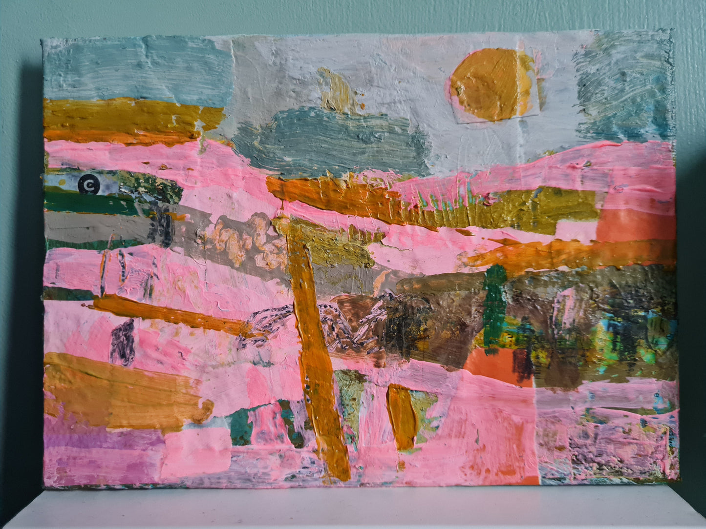 Abstract painting with pink, orange, and green colours on a white surface, and sage green background.