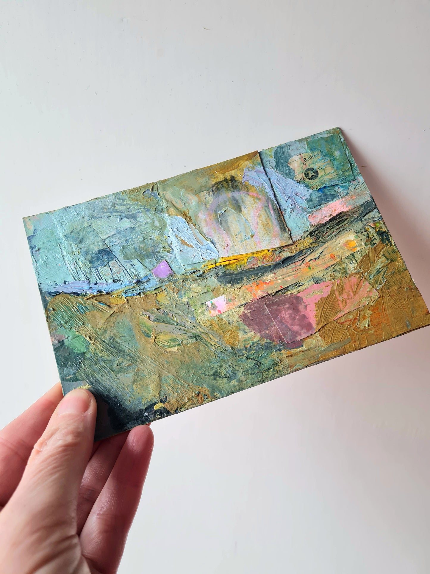 Hand holding a small abstract painting with muted colours on a white background