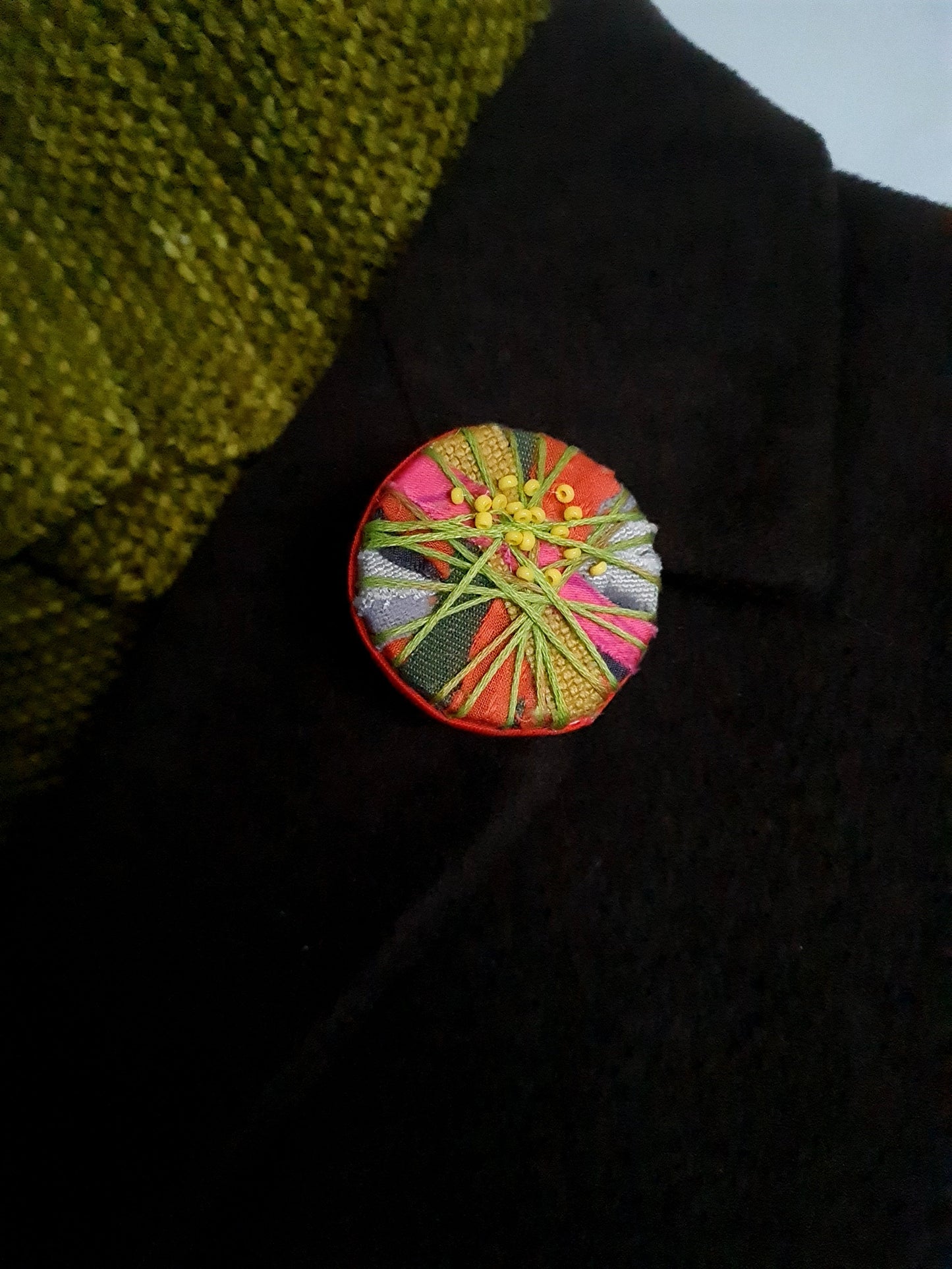Colourful textile-art statement brooch on the lapel of a dark coat