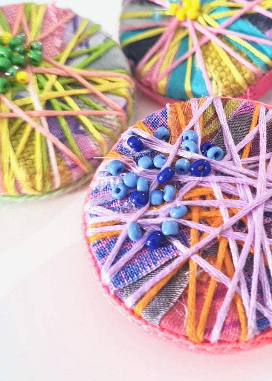 Colourful thread-wrapped statement brooches on a white background