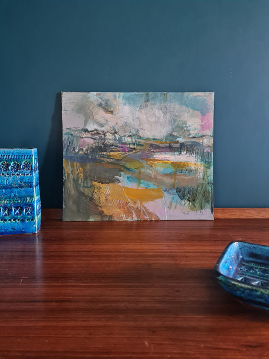 Abstract landscape painting on a dark wood surface with a Rimini blue craft pottery object in the corner.