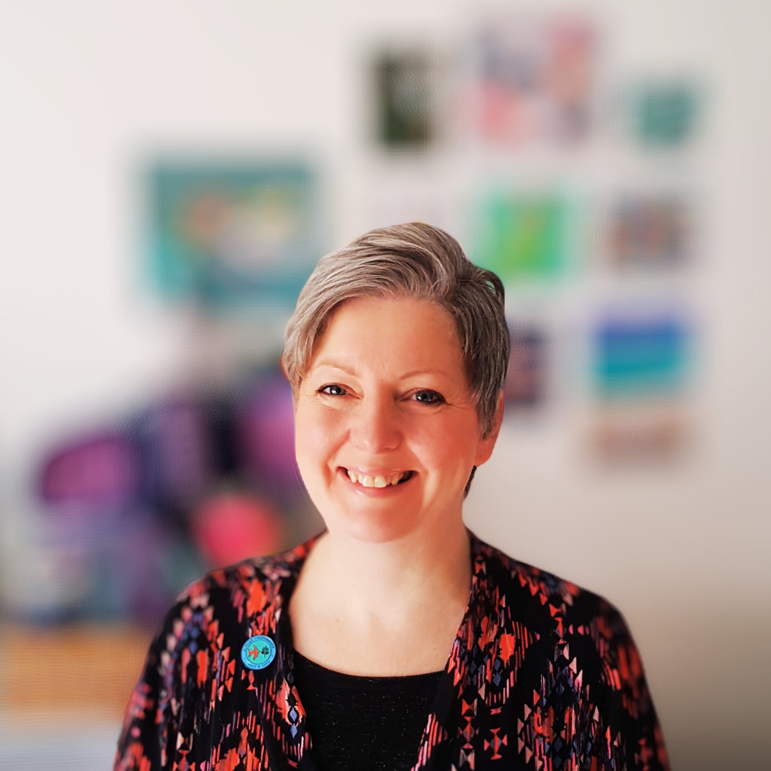 Photo of Julia Laing, artist and craft maker. She is pictured in her studio at home in Scotland. On her lapel is a #justacard pin badge.