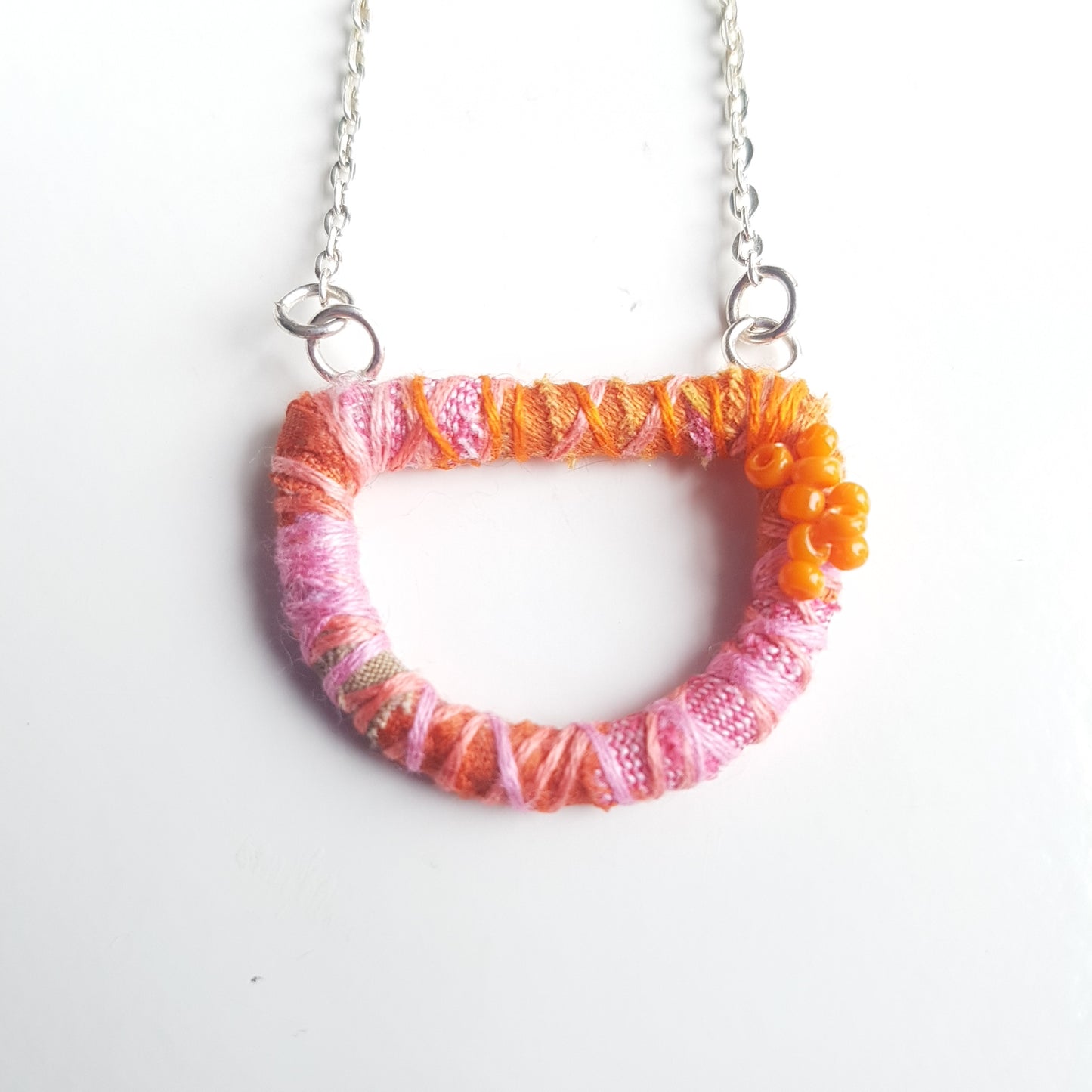 Pink and orange textile art necklace close up on a white table.