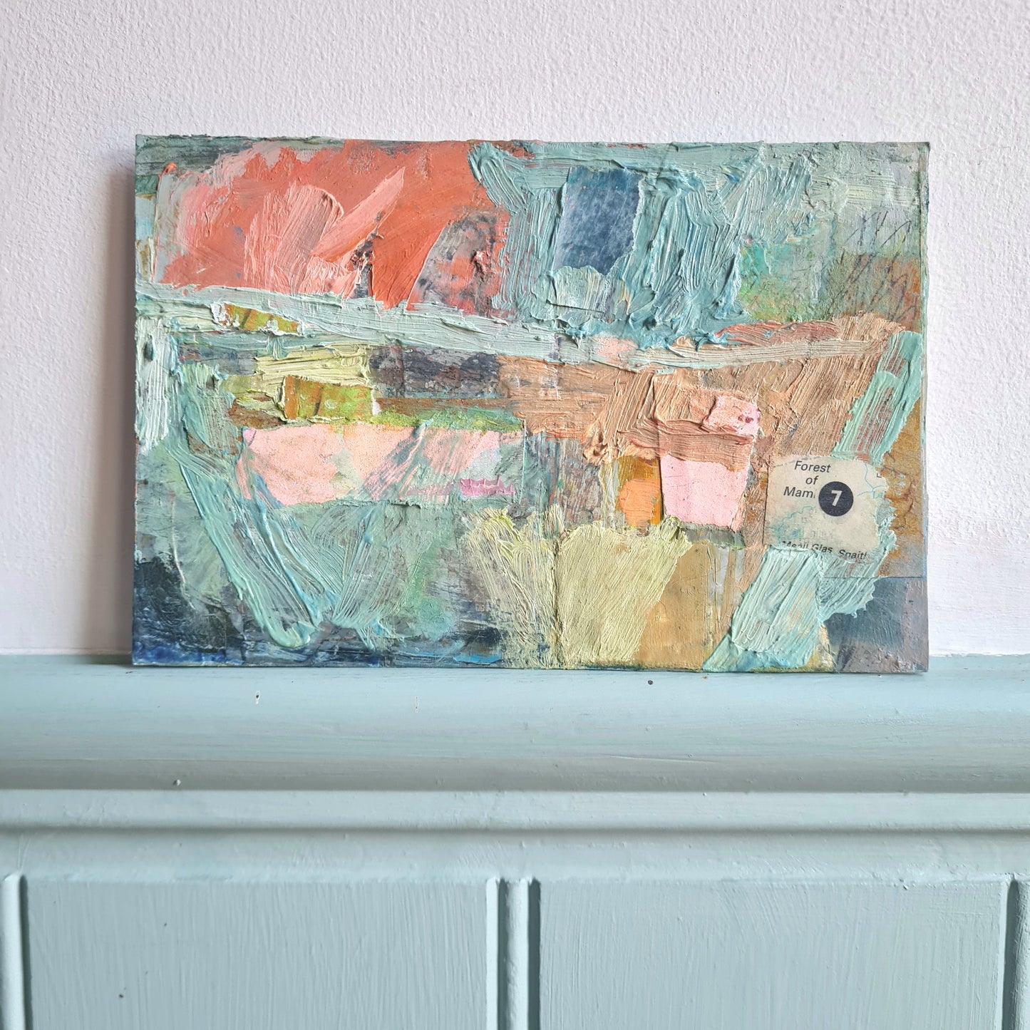 Abstract painting on a white wall above a light blue shelf