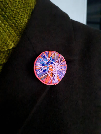 Colourful circular brooch on a dark fabric background