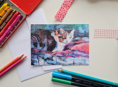 Colourful art greeting card with a cat design on a desk with coloured pencils and paper.