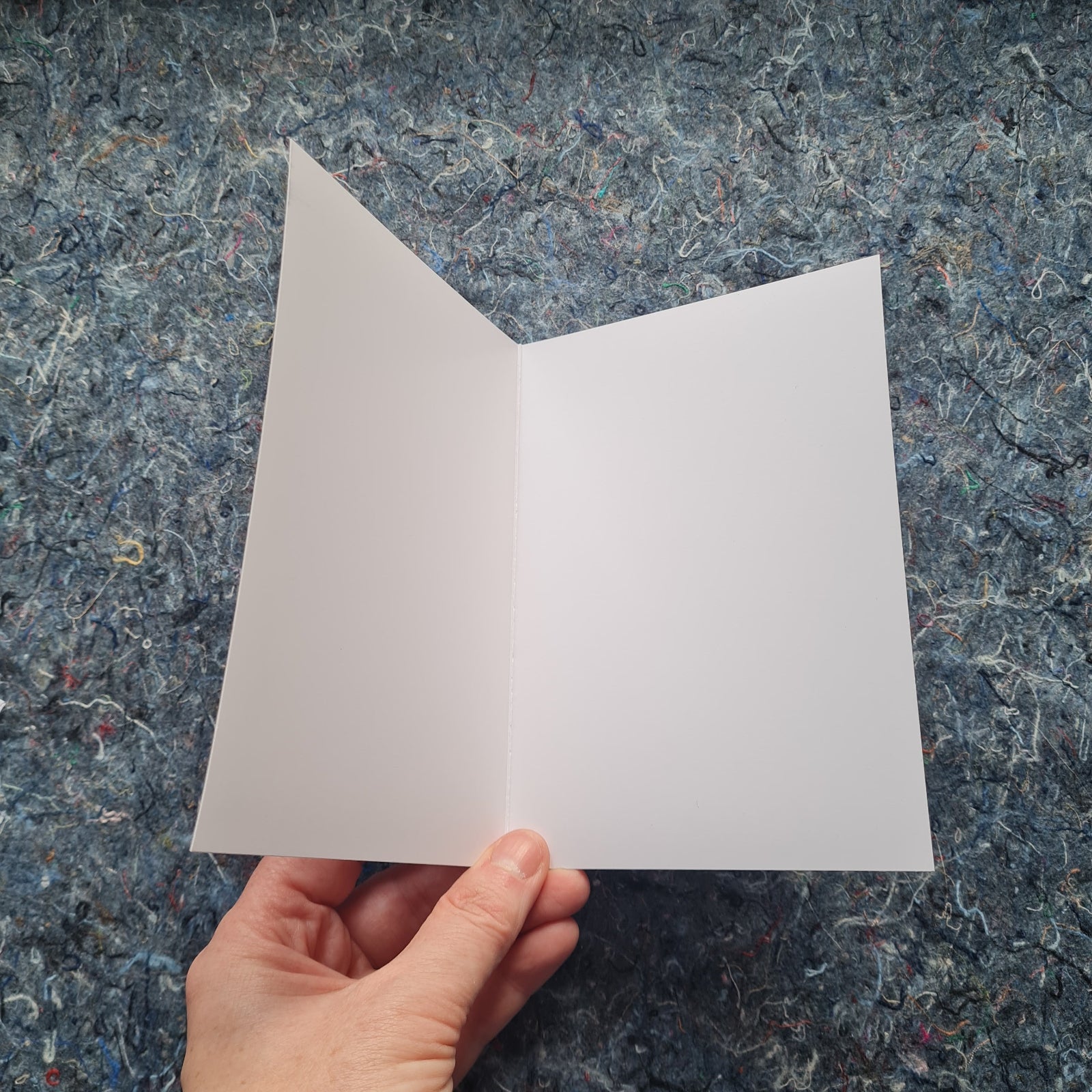 Hand holding a white card against a textured blue/grey background