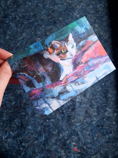 Hand holding a greeting card with a  painting of a cat on a textured dark surface
