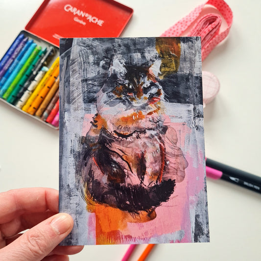 Cat painting greeting card held by a hand above a white table with coloured pencils and a box of crayons in the background