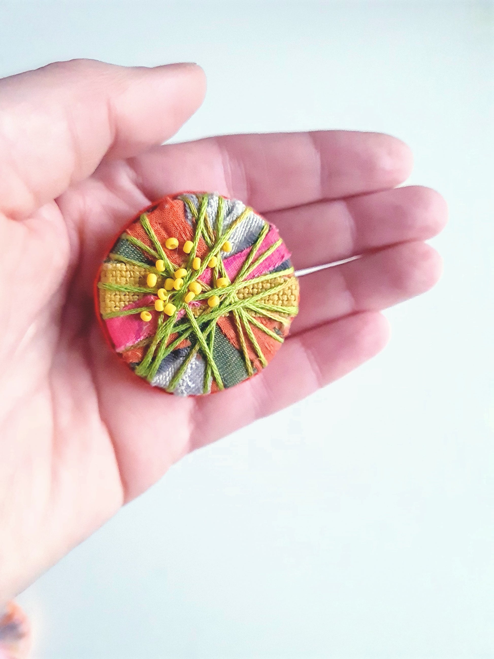 Colourful embroidered brooch held in a hand against a light background