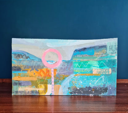 Colourful abstract painting on a dark wood surface with a teal blue wall behind it