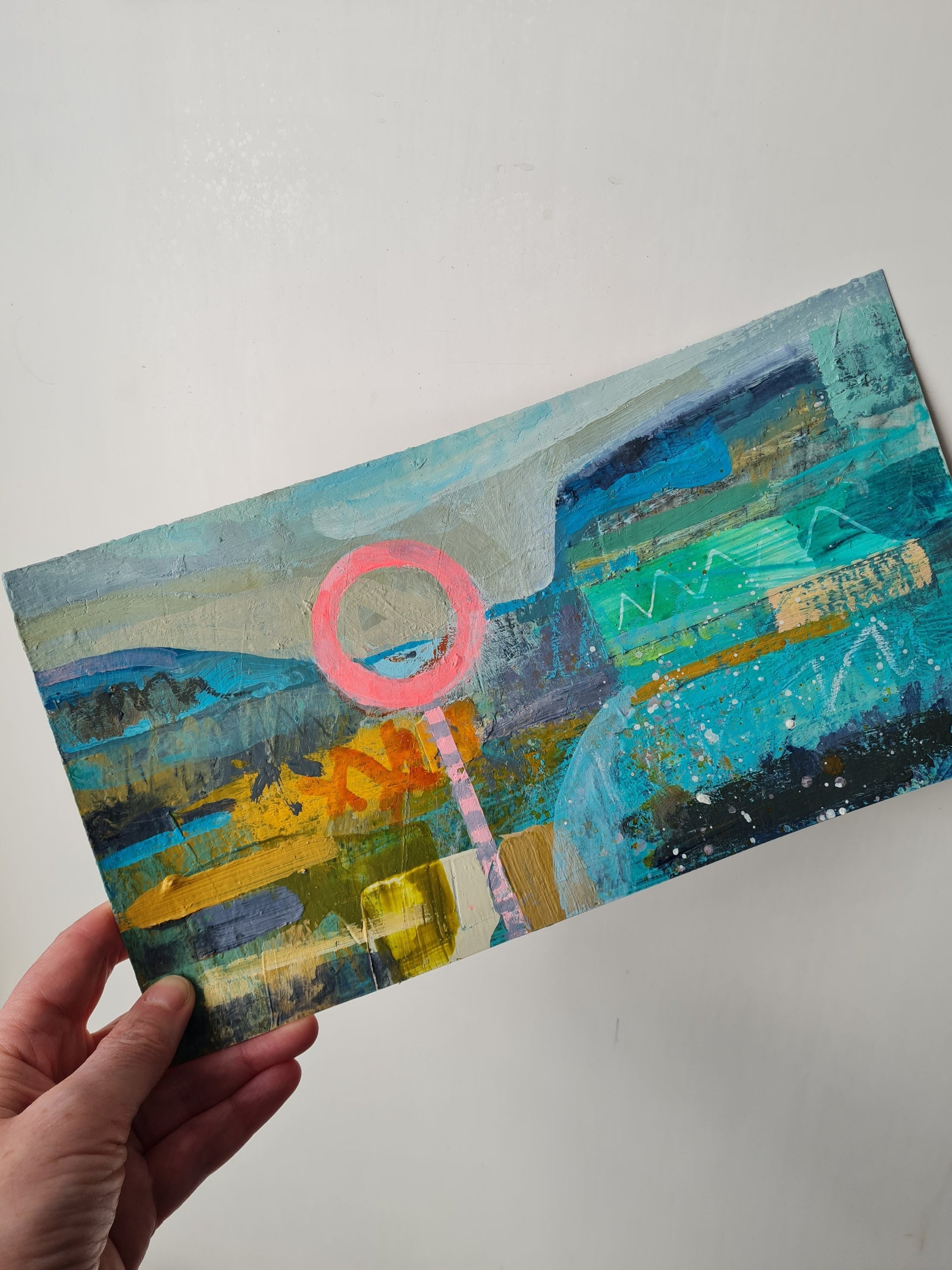 Colourful abstract painting held by a hand on a white background