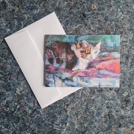 Colourful cat illustration on a card with a white envelope on a textured surface