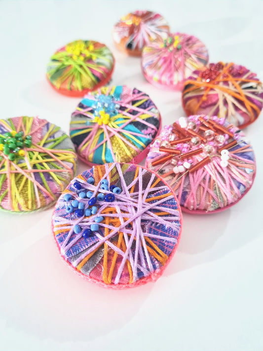 colourful circular textile art statement brooches lying in a group on a white background