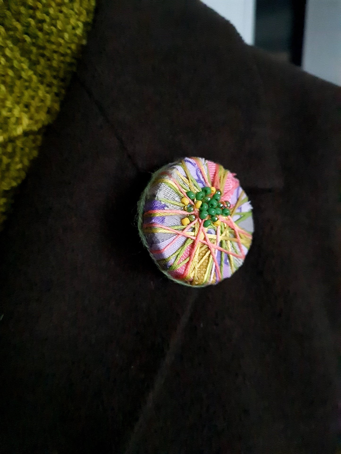 colourful artisan statement brooch on the lapel of a dark coat