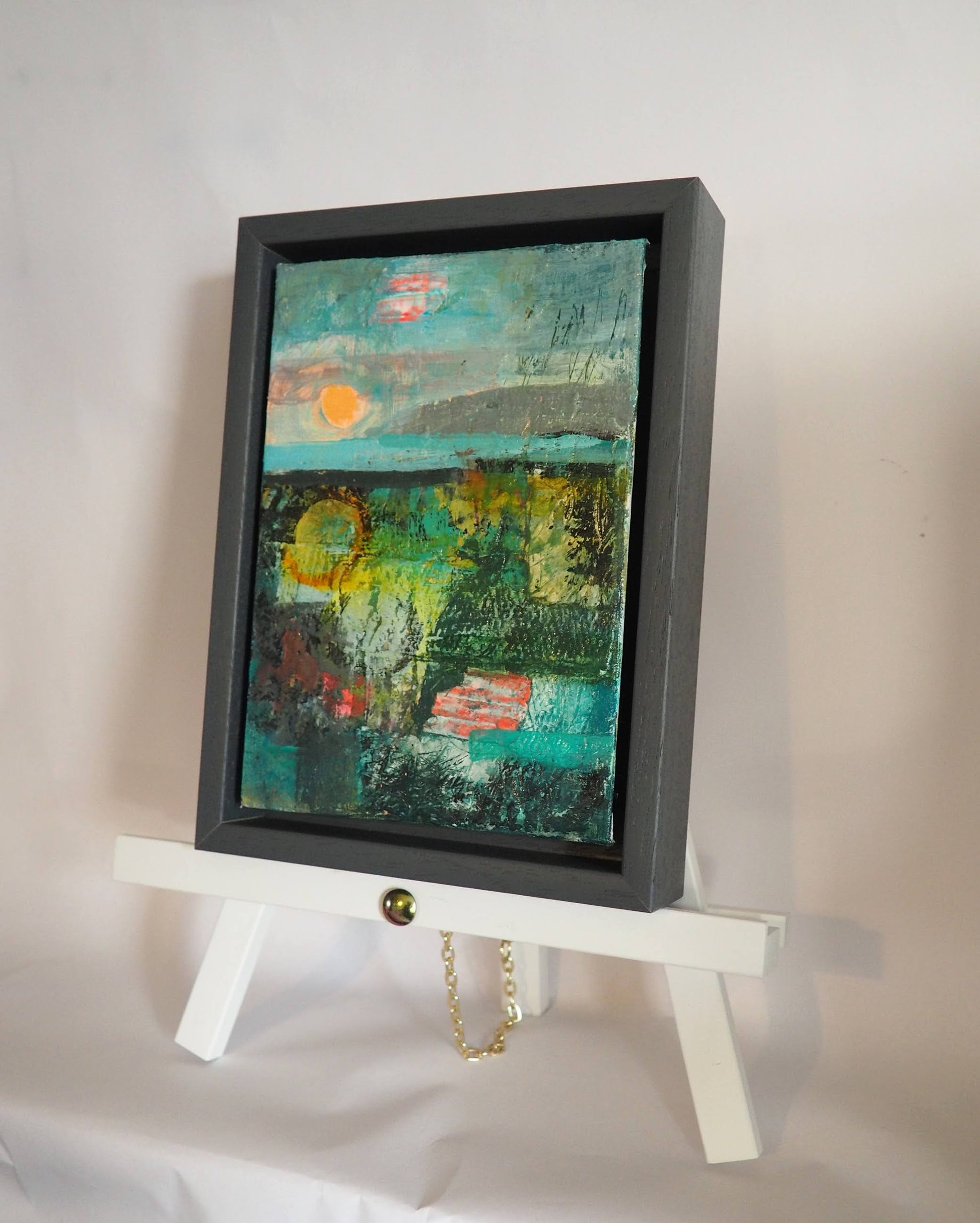 Small framed abstract landscape on a white tabletop easel against a white background.