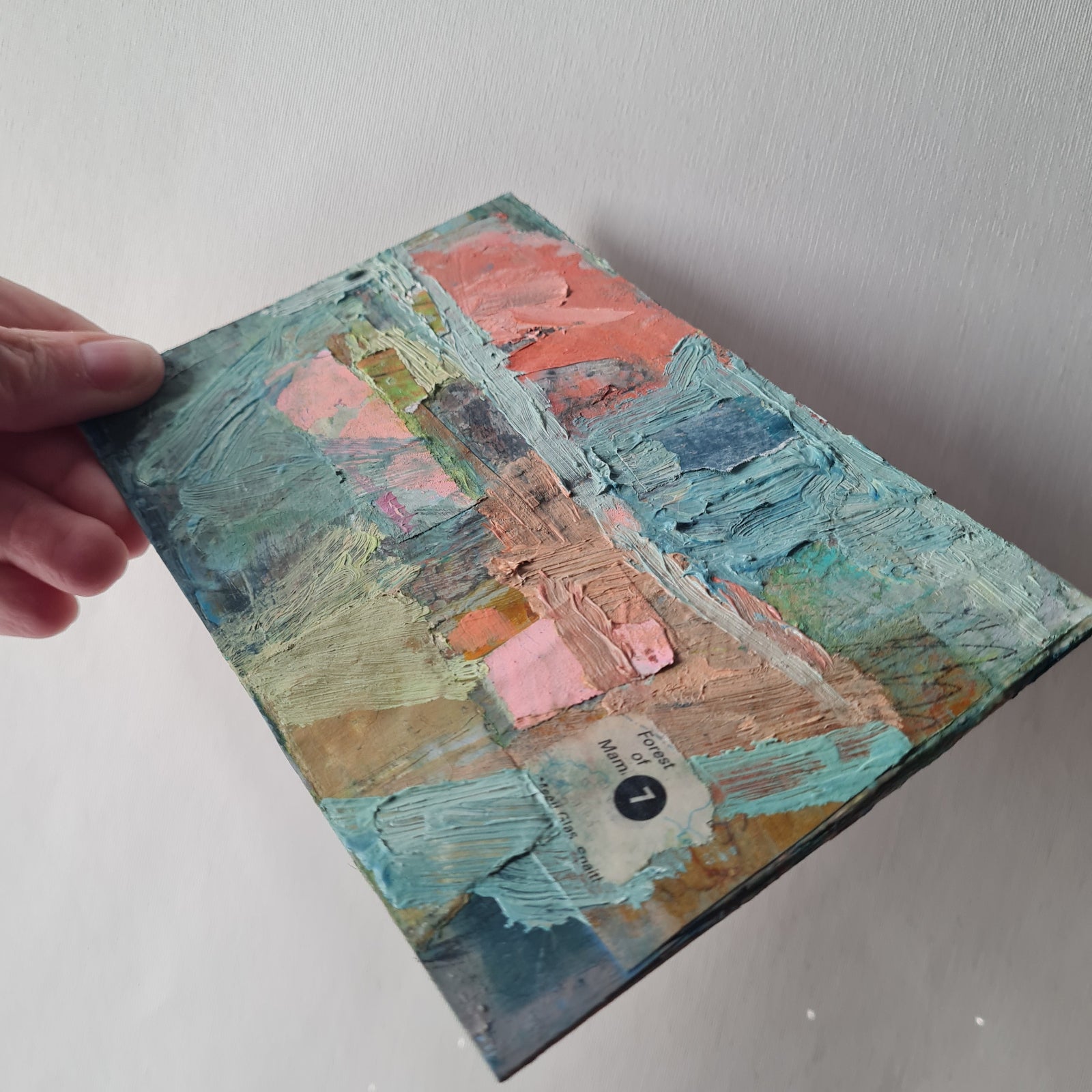 Small postcard-sized painting with textured brushstrokes, held by a hand on a light background.