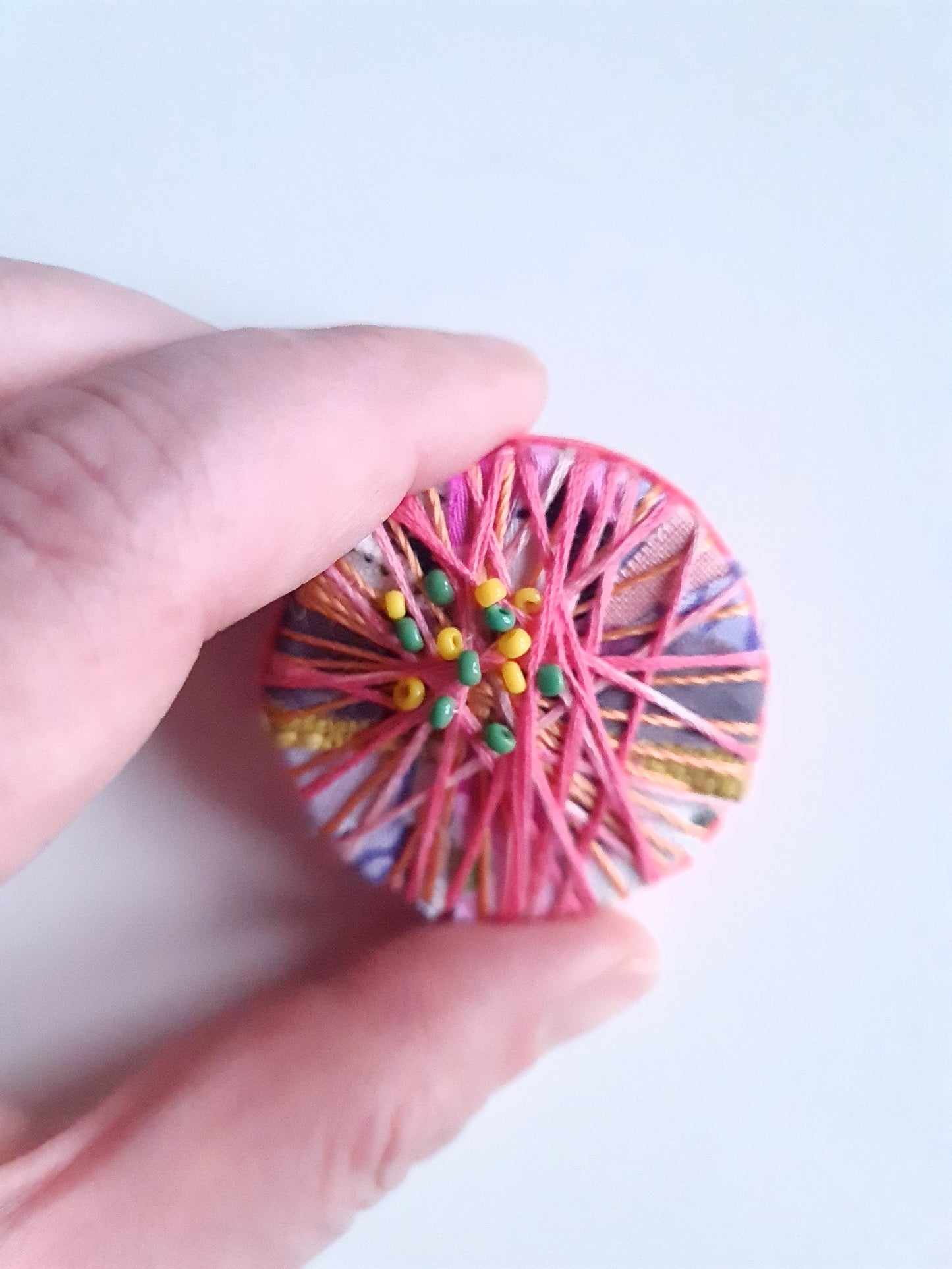 Hand holding a colourful textile art brooch against a light background