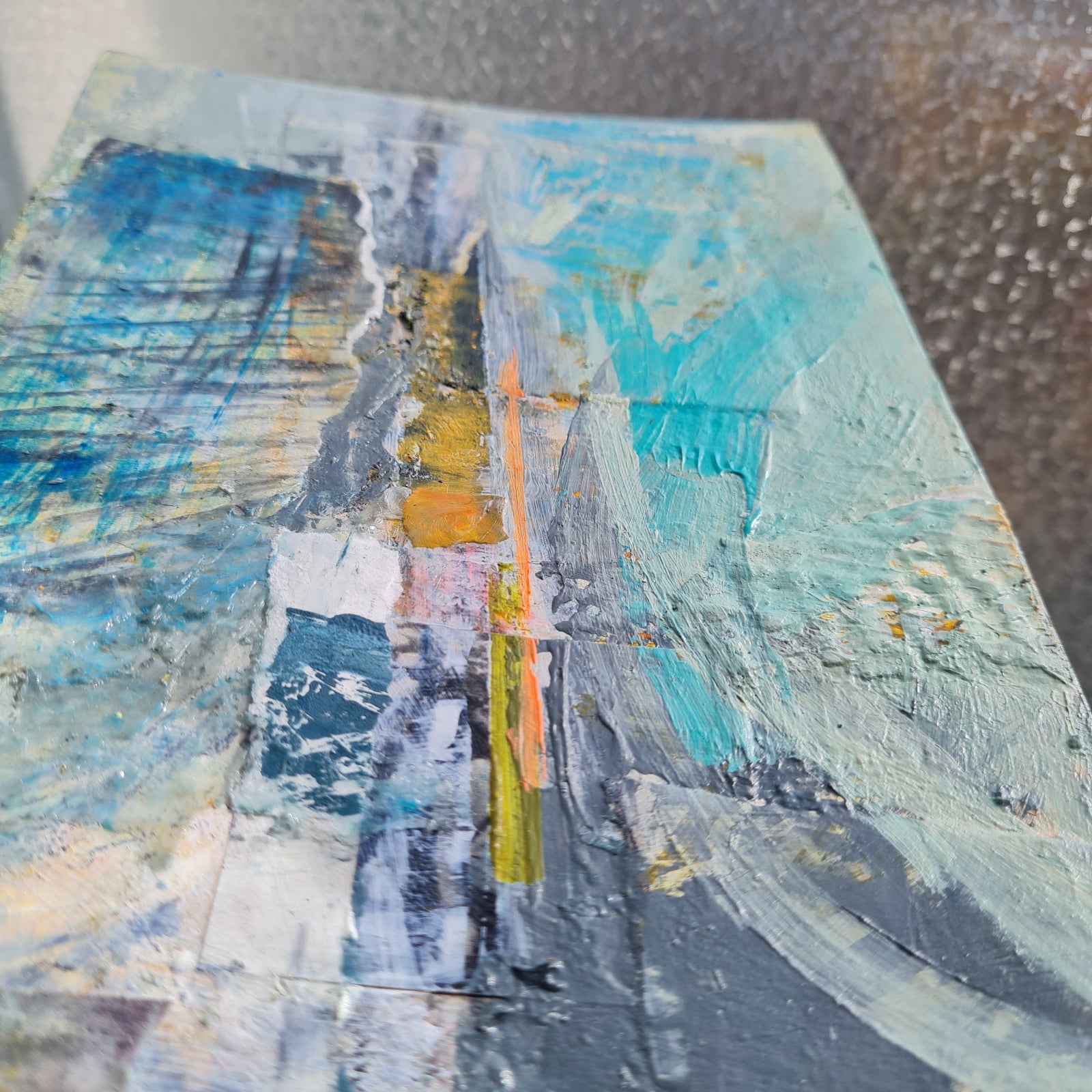 Abstract art piece with blue, gray, and yellow colors on a textured surface.