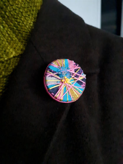 colourful textile art statement brooch on the lapel of a dark coat