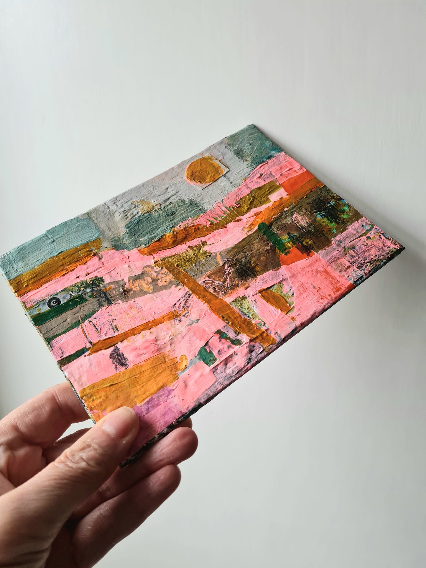Hand holding a small rectangular painting with abstract design on a white background
