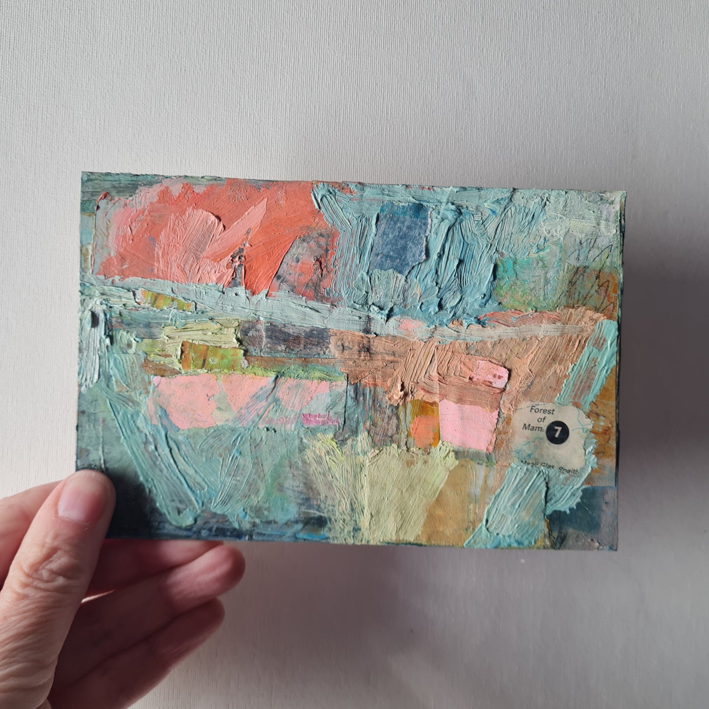 Hand holding a textured art piece with pastel colors on a neutral background