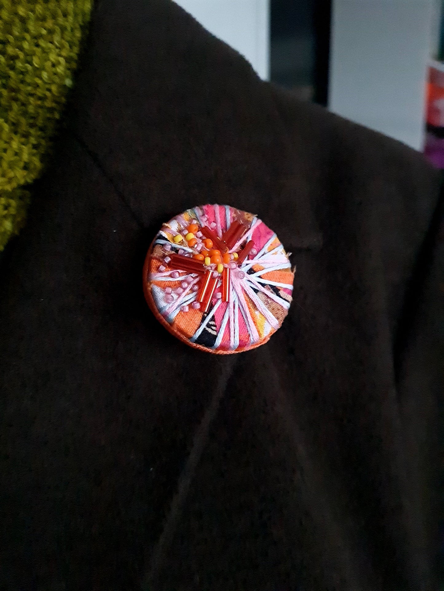 Colourful circular textile brooch on a dark coat lapel