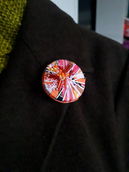 Colourful circular textile brooch on a dark coat lapel