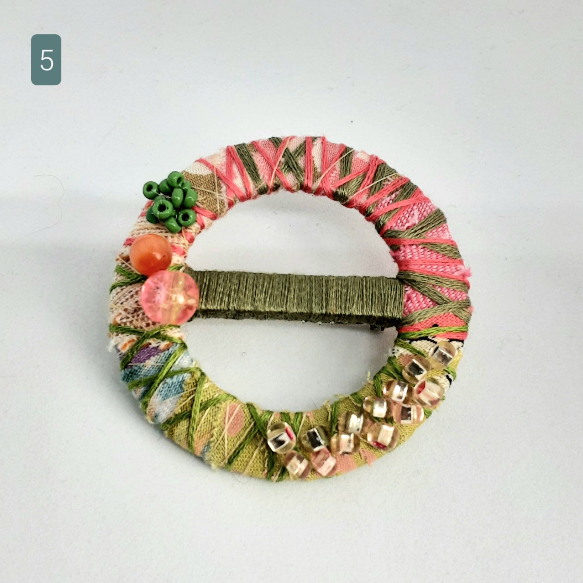 Circular statement textile brooch with bead embellishments on a white background