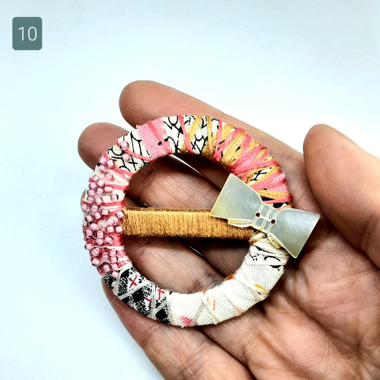 Hand holding cream and pink textile statement brooch. Background is white.