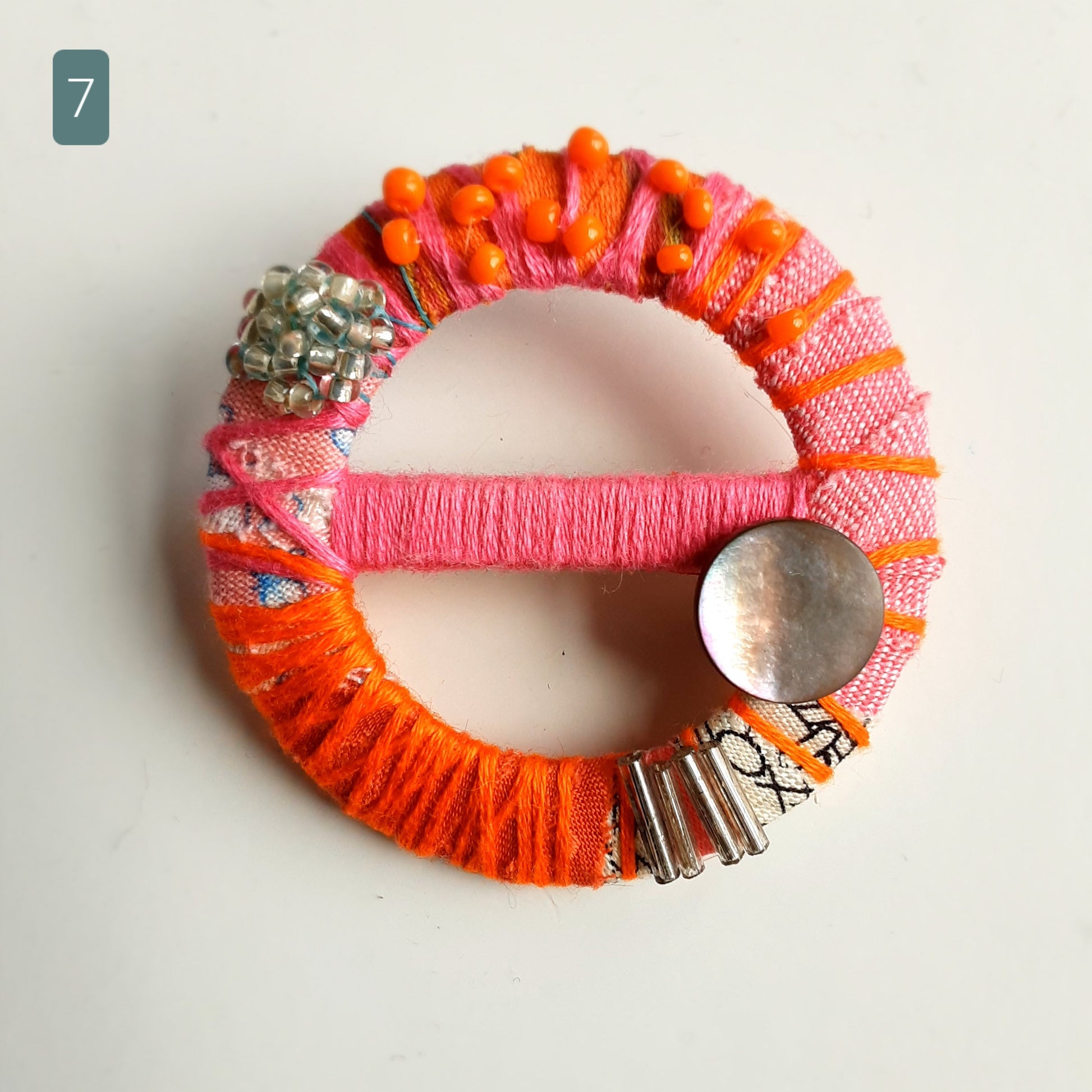 Beautiful statement textile brooch made from pink and orange fabrics and threads. Background is white.