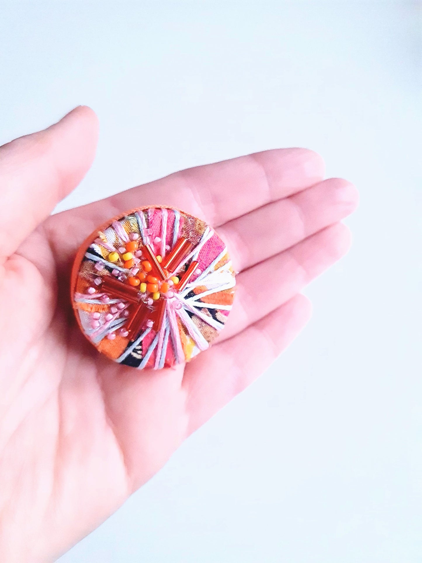 Colourful circular brooch held in a hand against a light background