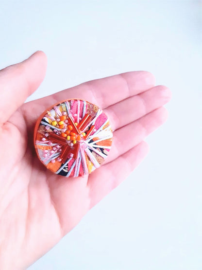 Colourful circular brooch held in a hand against a light background