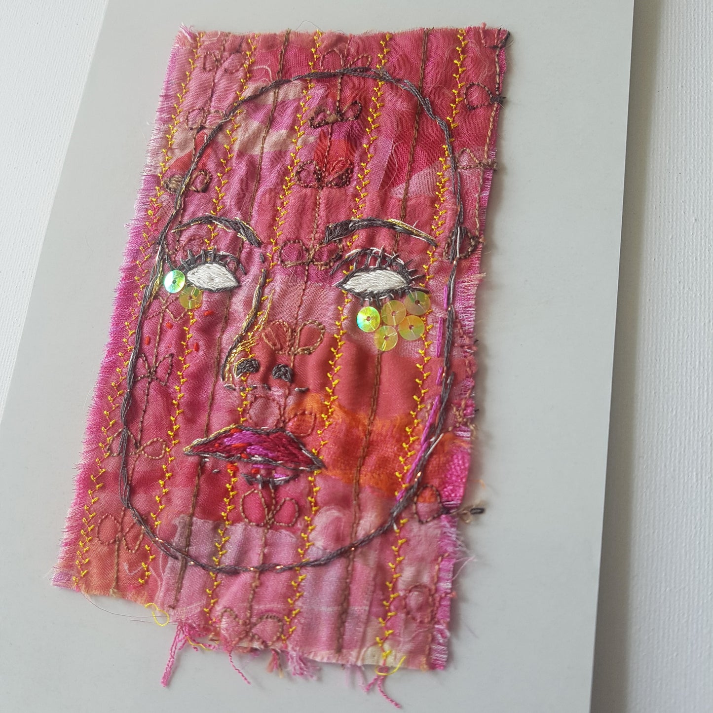 Textile artwork. Red embroidered face called Who is Behind the Mask? 