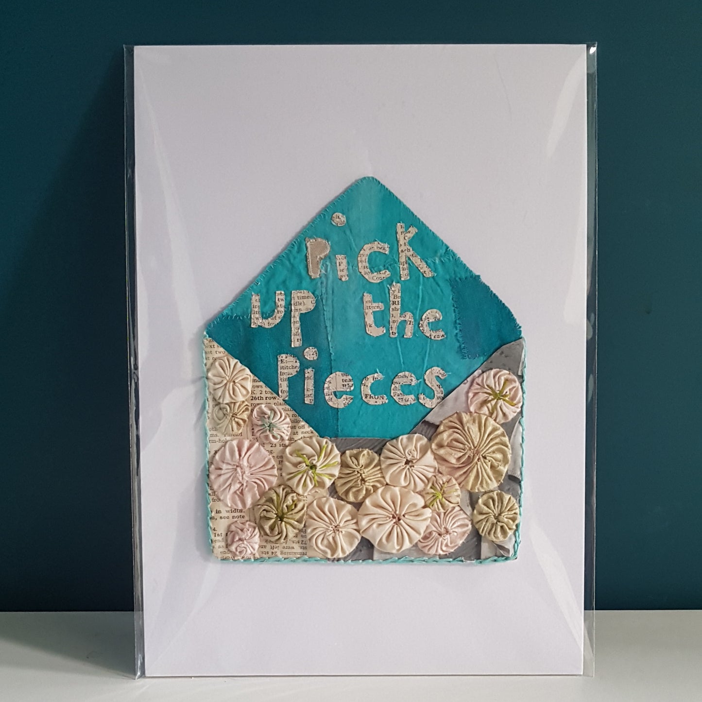 small cream textile art envelope with turquoise fabric inside and the words pick up the pieces written in paper applique.