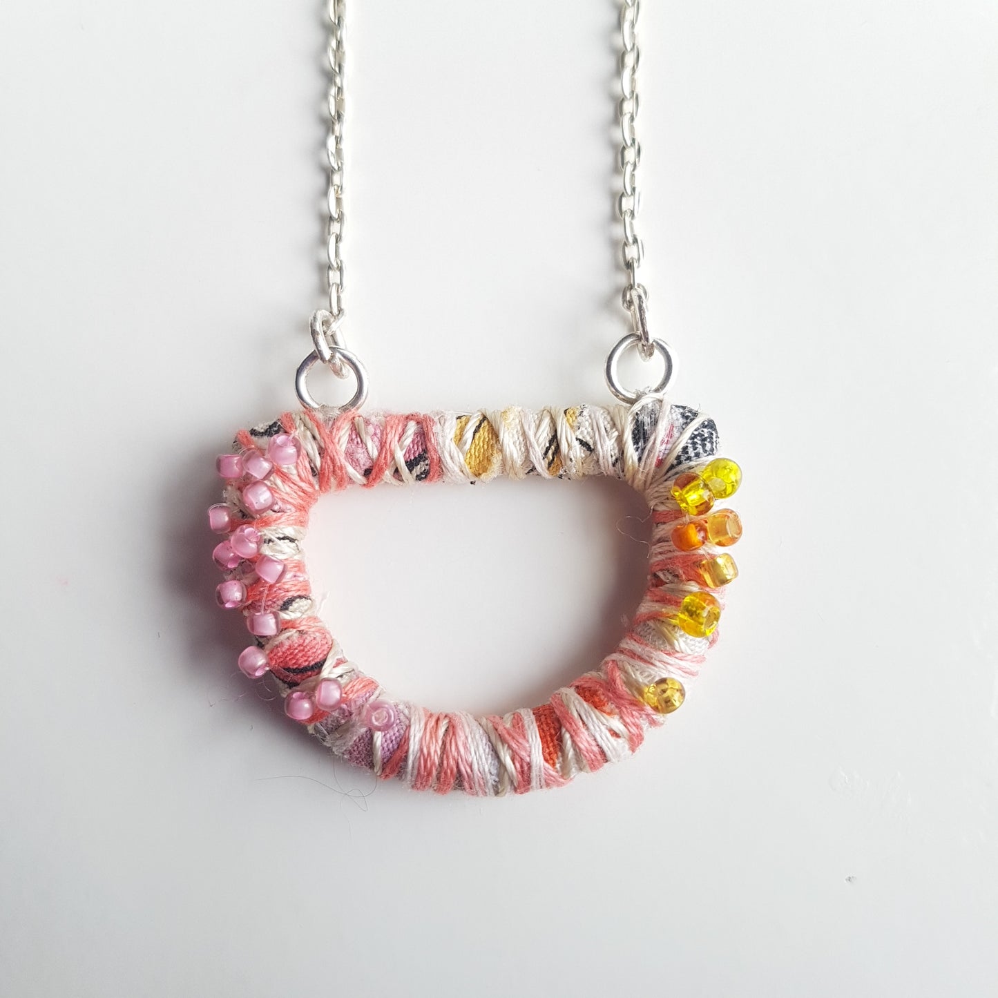 Pale pink and cream textile art necklace against a white background.