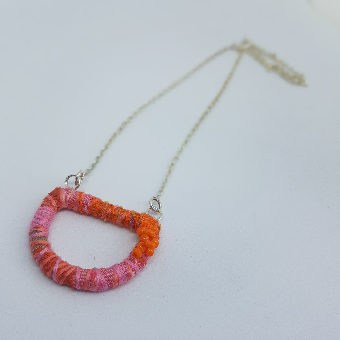 Orange and pink textile art necklace lying on a white table top