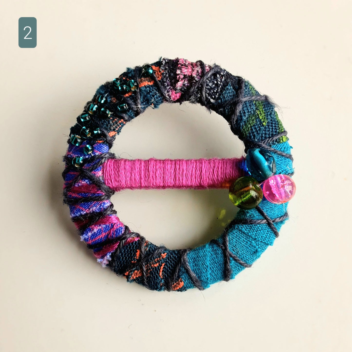 Teal and magenta textile brooch on a white background.