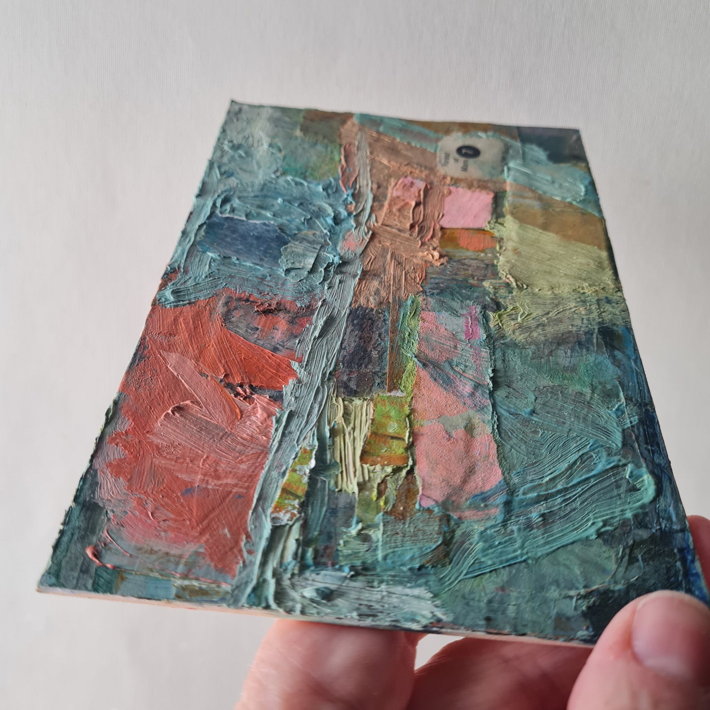 Hand holding a small textured painting with a landscape scene.
