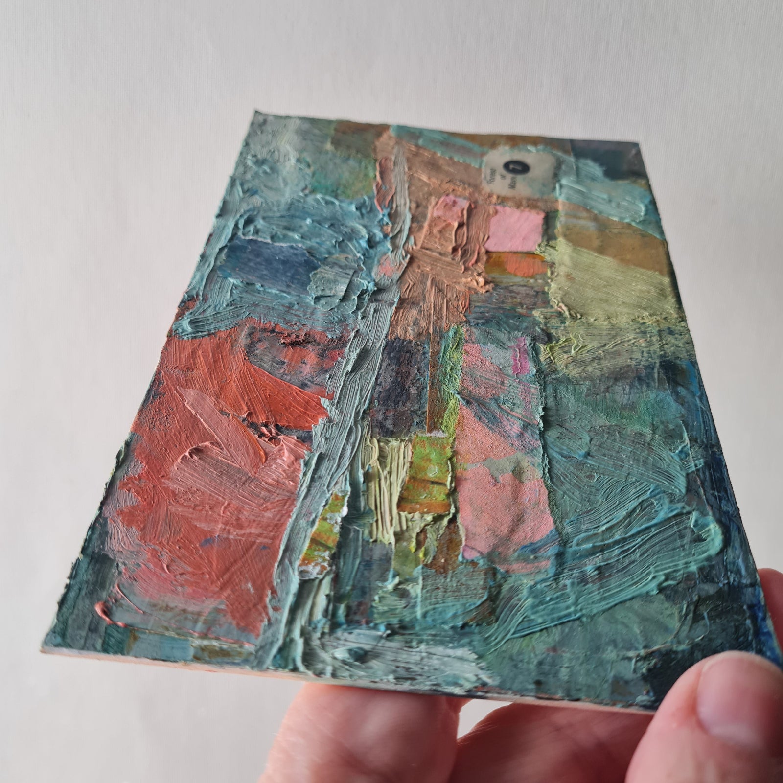 Hand holding a small textured painting with a landscape scene.