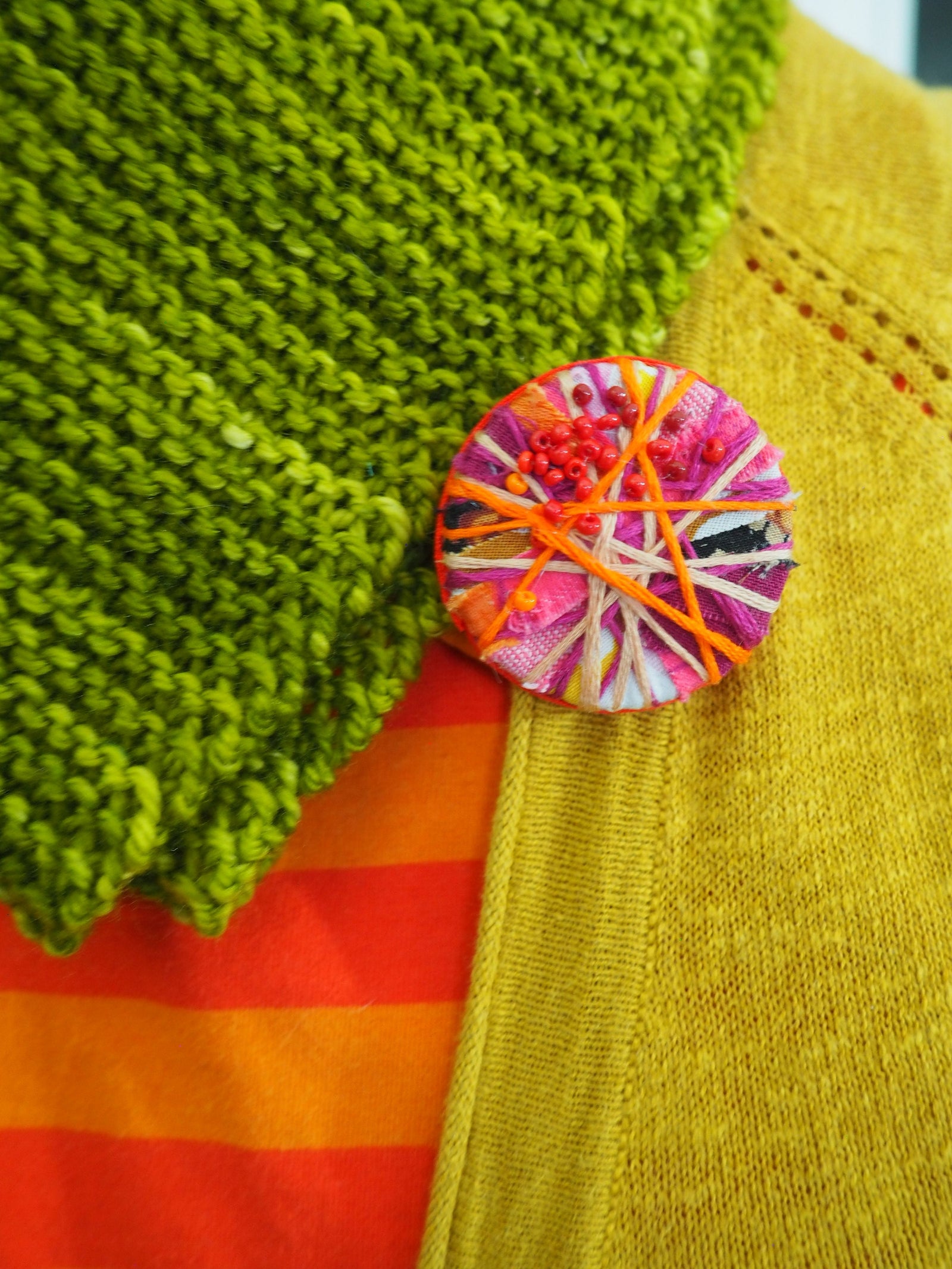 Close-up of a colourful brooch on fabric with green, red, and yellow patterns.