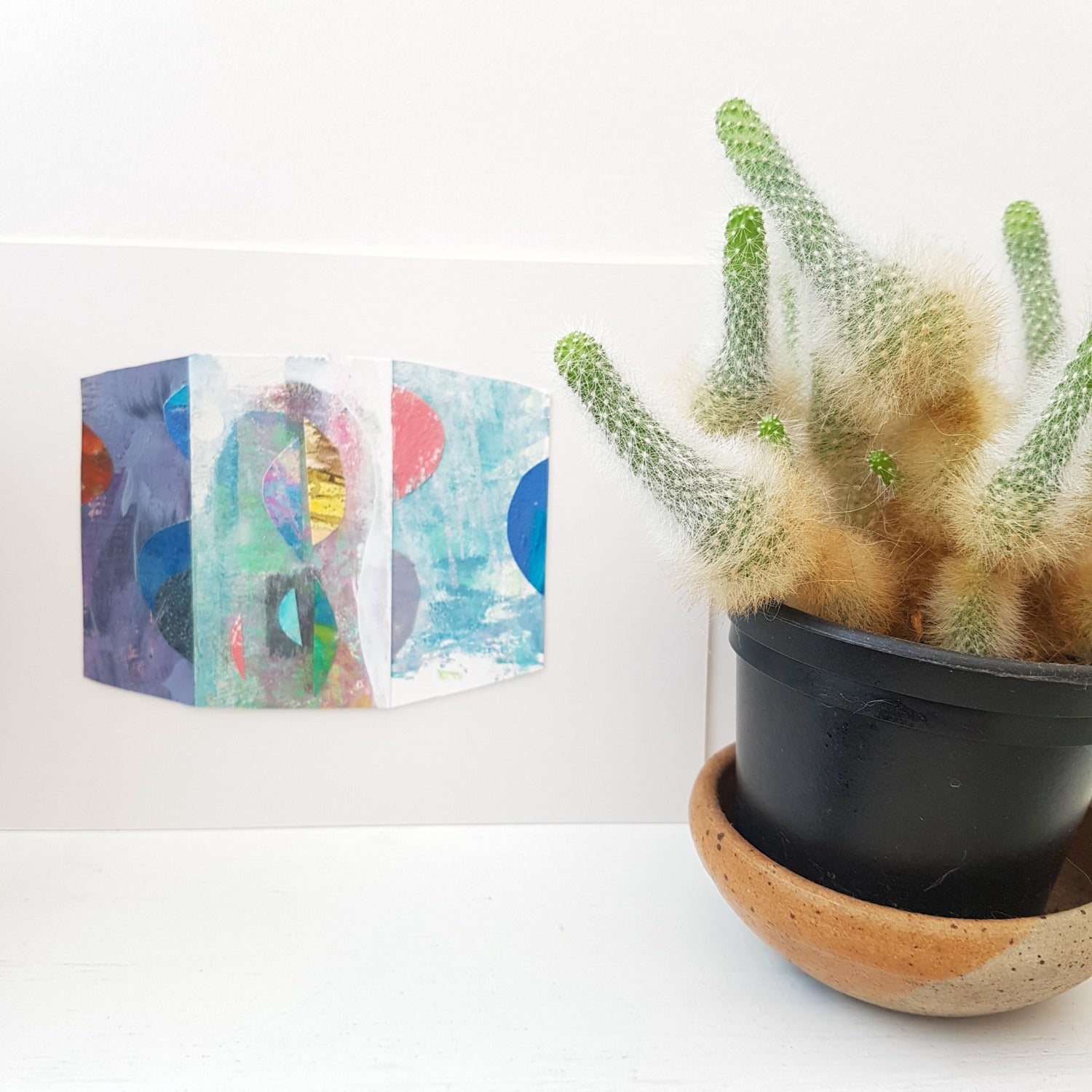 Collage by Julia Laing on a shelf beside a succulent plant.