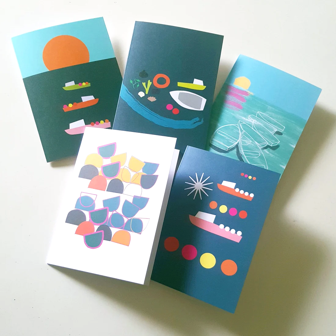 Set of greeting cards on a white background. 5 different modern seascape designs with boats and floats, lobster pots and  colourful seashore scenes by UK indie designer Julia Laing.